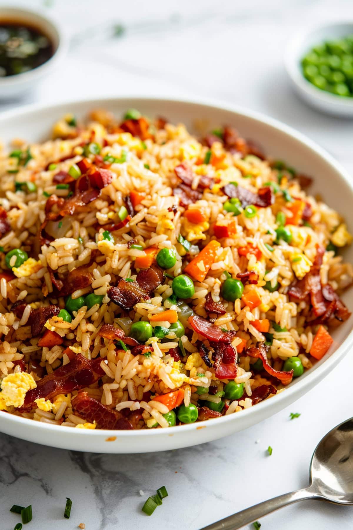 Fried rice with bacon, green peas, carrots in soy sauce served in a white plate.