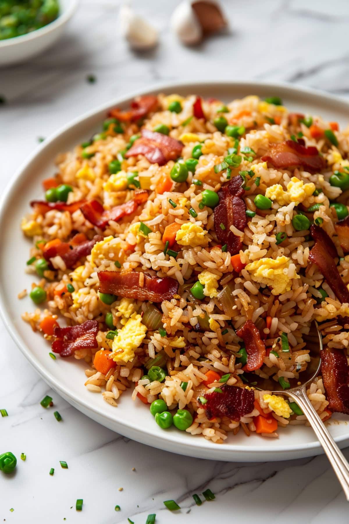 Fried rice with bacon served in a white plate with spoon.