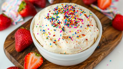 Fun and festive funfetti cake dip in a white bowl, served with fresh strawberries on the side