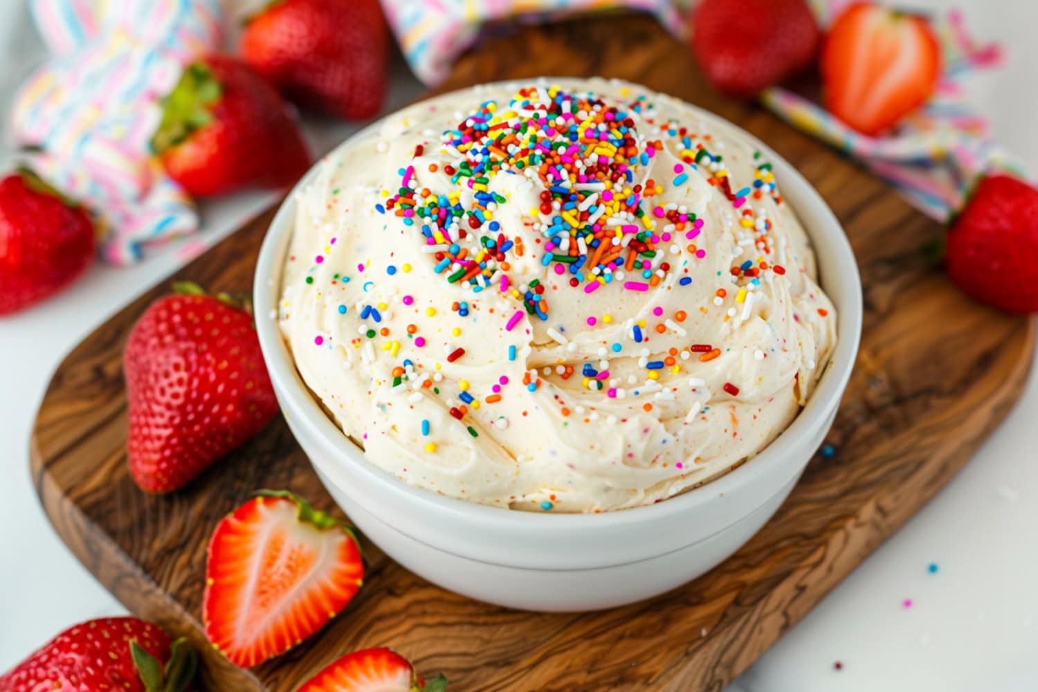 Fun and festive funfetti cake dip in a white bowl, served with fresh strawberries on the side