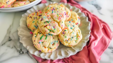 Quick and easy cake mix cookies in a white plate loaded with sprinkles.