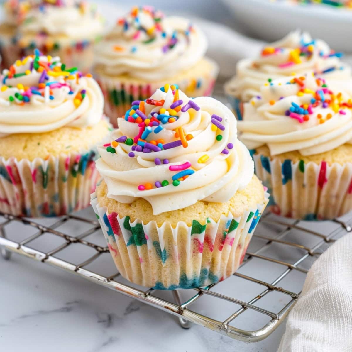Soft and fluffy funfetti cupcakes topped with buttercream and sprinkles in a cooling rack
