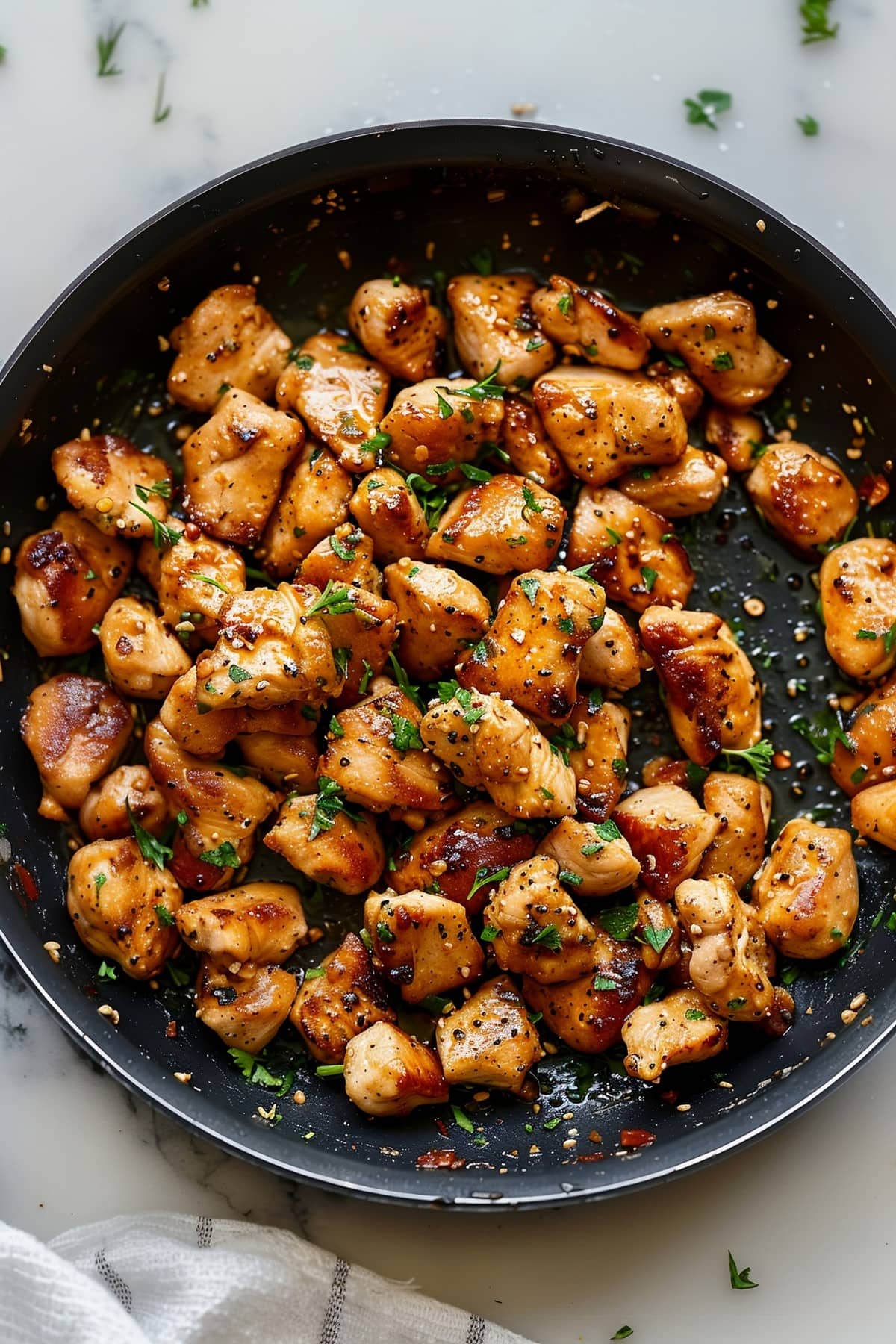 Savory garlic butter chicken bites with Italian seasoning and parsley in a black skillet, overhead view