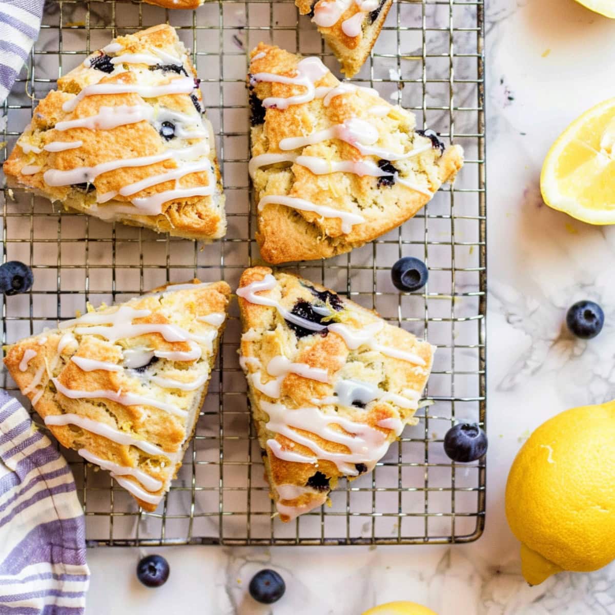 Overhead view of blueberry scones topped with lemon glaze on a white marble countertop.