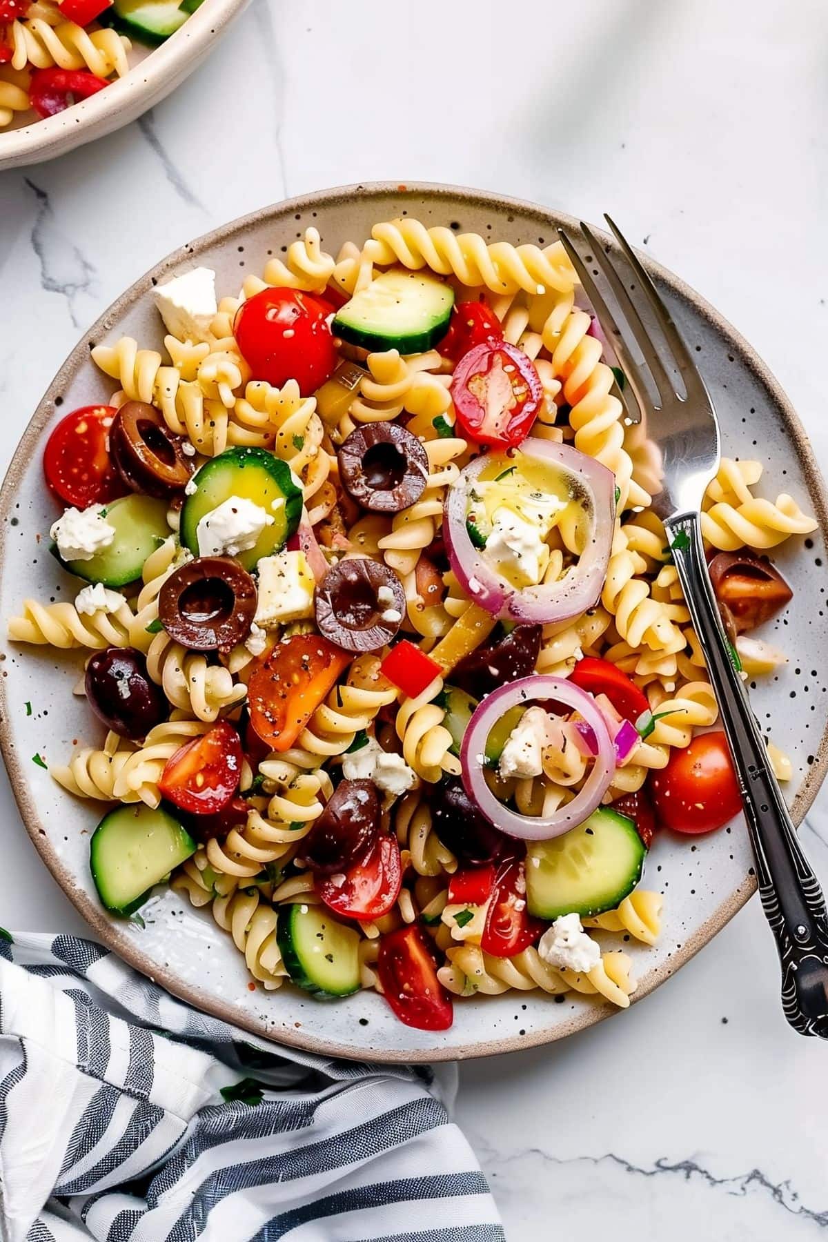 Greek Pasta Salad with Rotini, Black Olives, Red Onion, Cucumber, Tomatoes, and Feta Cheese on a Plate with a Fork