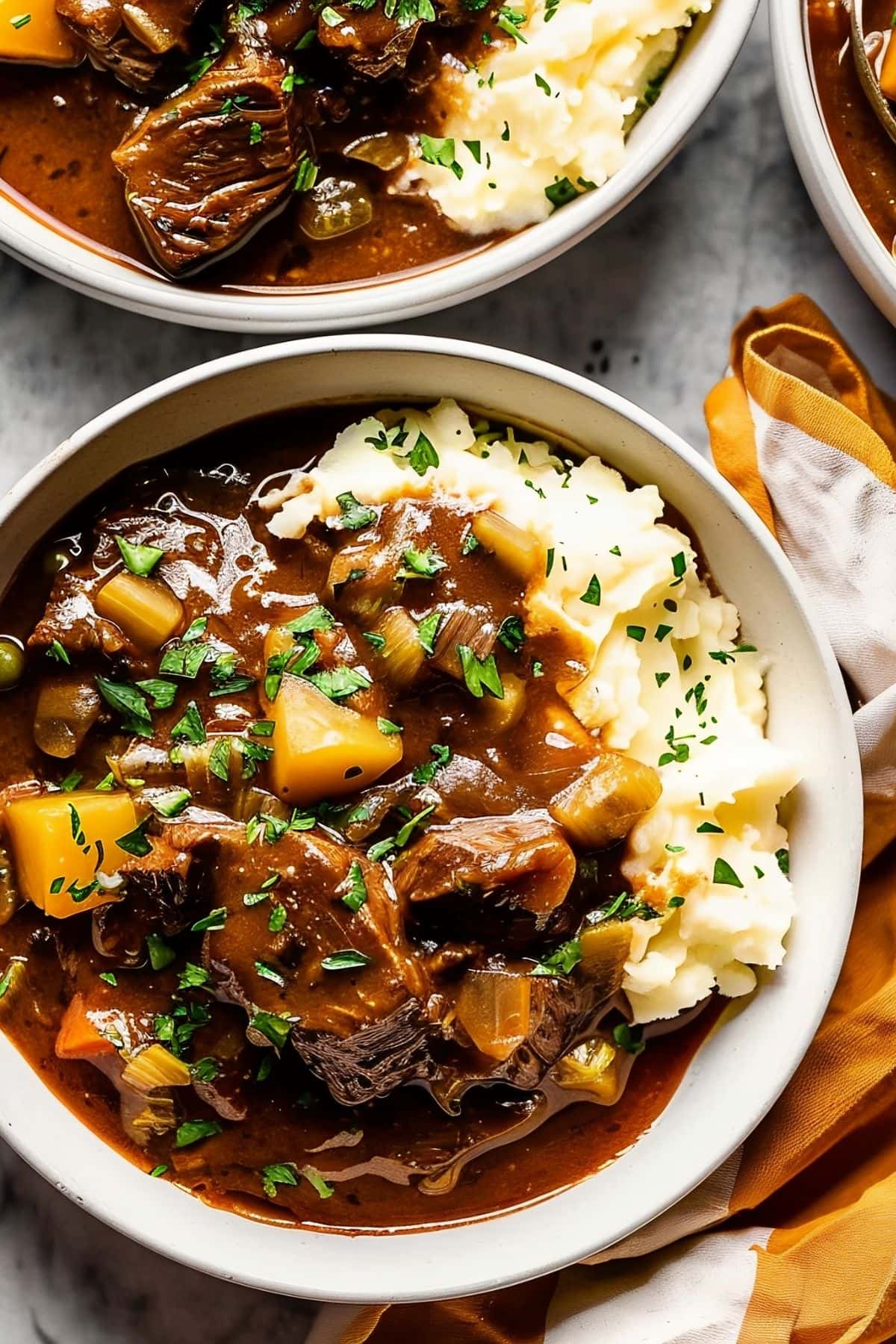 Three Bowls of Delicious Guinness Beef Stew Over Mashed Potatoes with a Yellow Kitchen Towels