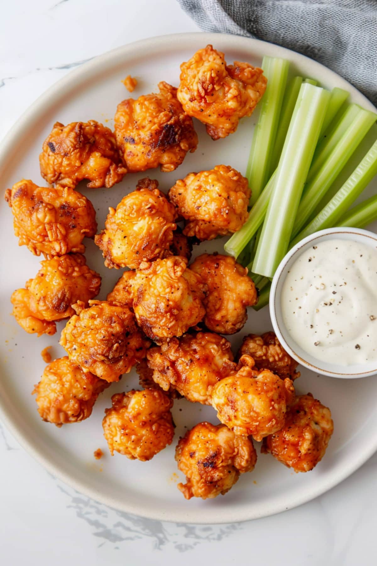 Spicy buffalo chicken bites on a white plate with celery sticks and ranch dressing