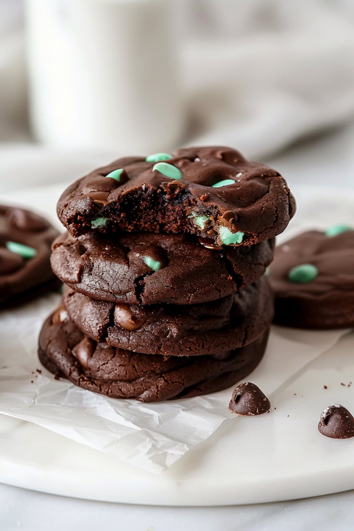 Chocolatey and chewy homemade chocolate mint chip cookies stacked on parchment paper on a white marble countertop.