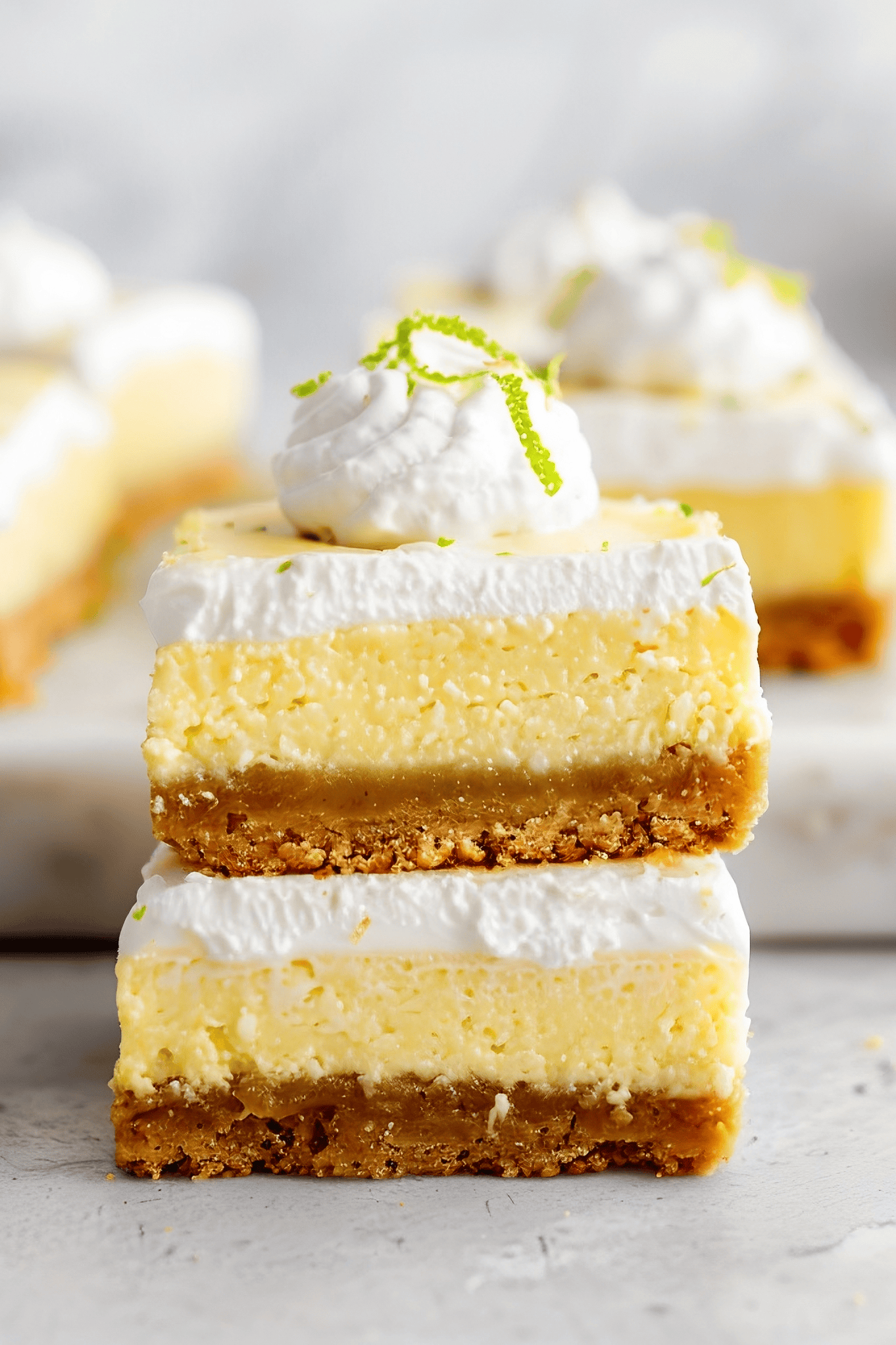 Two slices of key lime pie bars stacked with whipped cream and lime zest on top