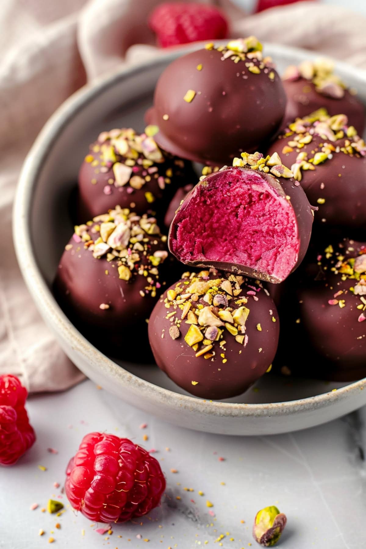 A bowl of white chocolate raspberry truffles coated in dark chocolate and topped with pistachio nuts