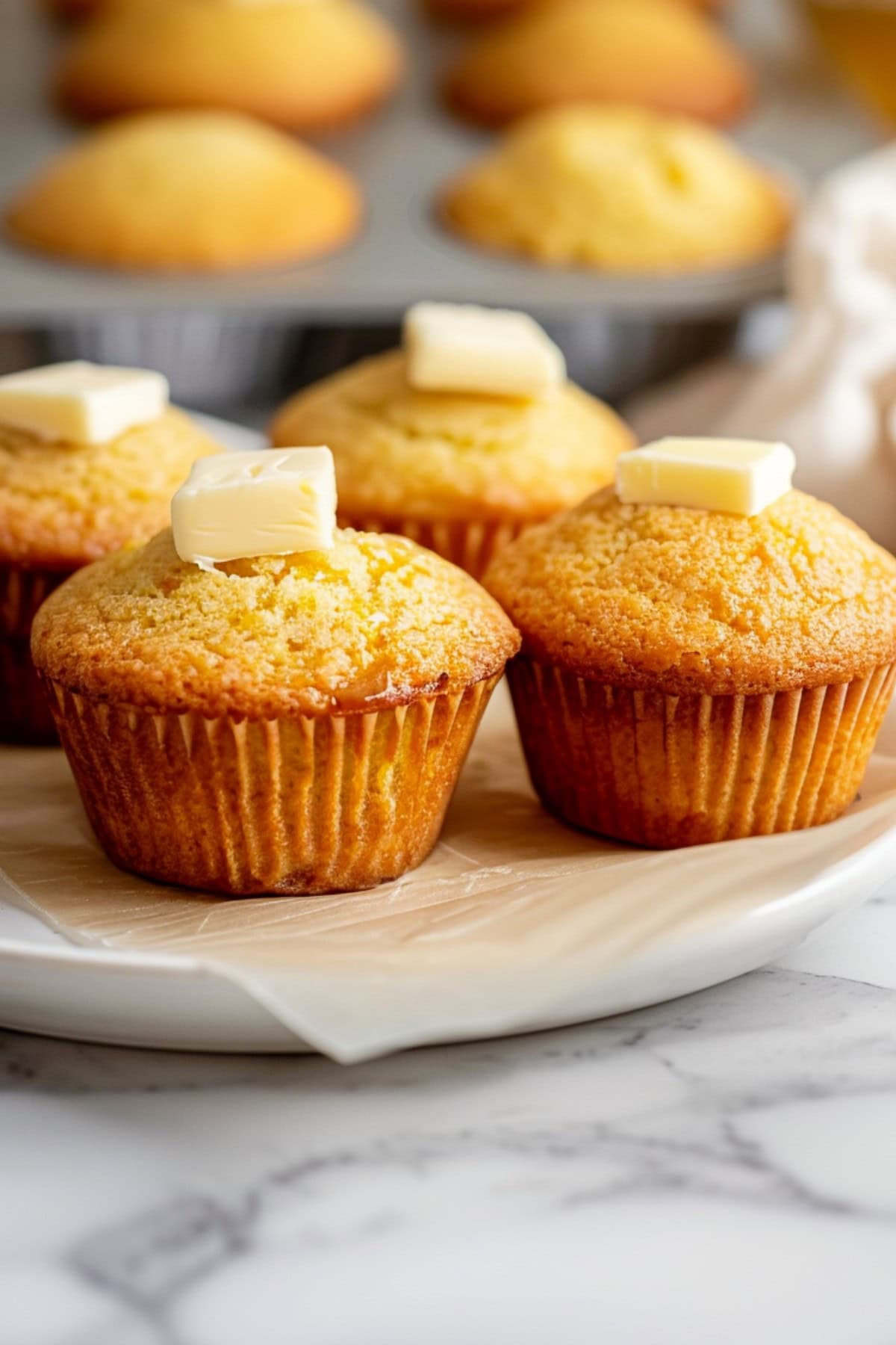 Honey cornbread muffins topped with unsalted butter in a white plate
