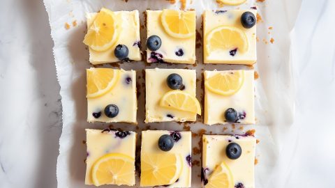 Lemon blueberry cheesecake bars arranged neatly on a white parchment paper.