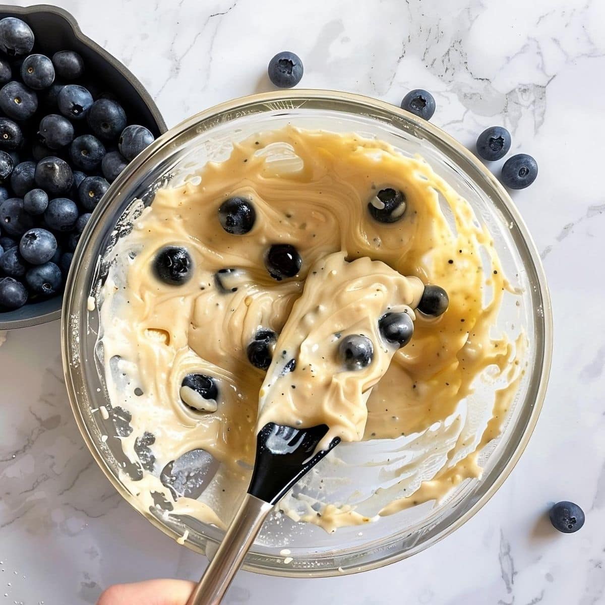 Top View of Lemon Blueberry Muffin Batter with Fresh Blueberries in a Glass Bowl on a White Marble Table with a Bowl of Blueberries to the Side
