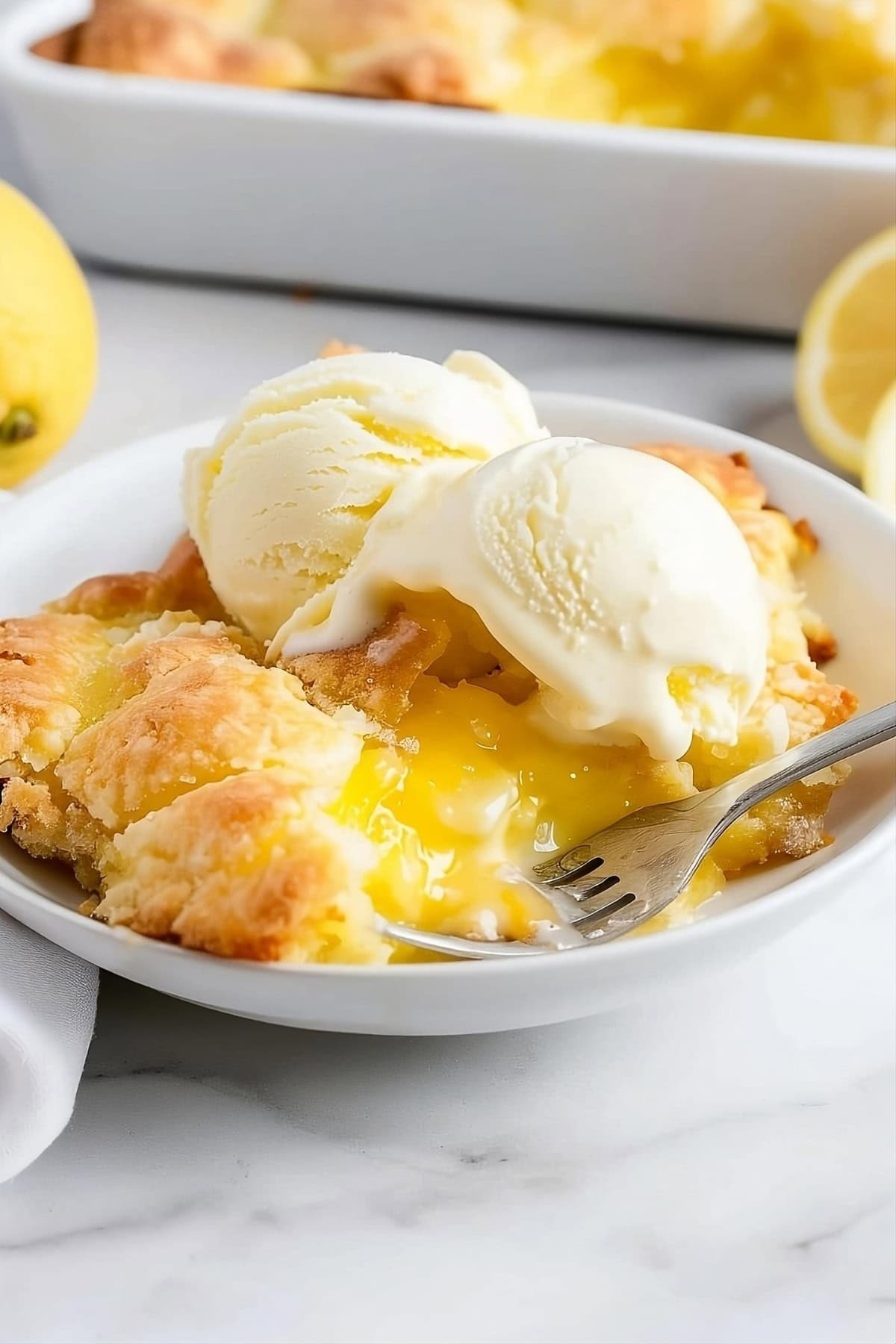 Lemon cobbler serving in a white plate garnished with two scoops of vanilla ice cream.