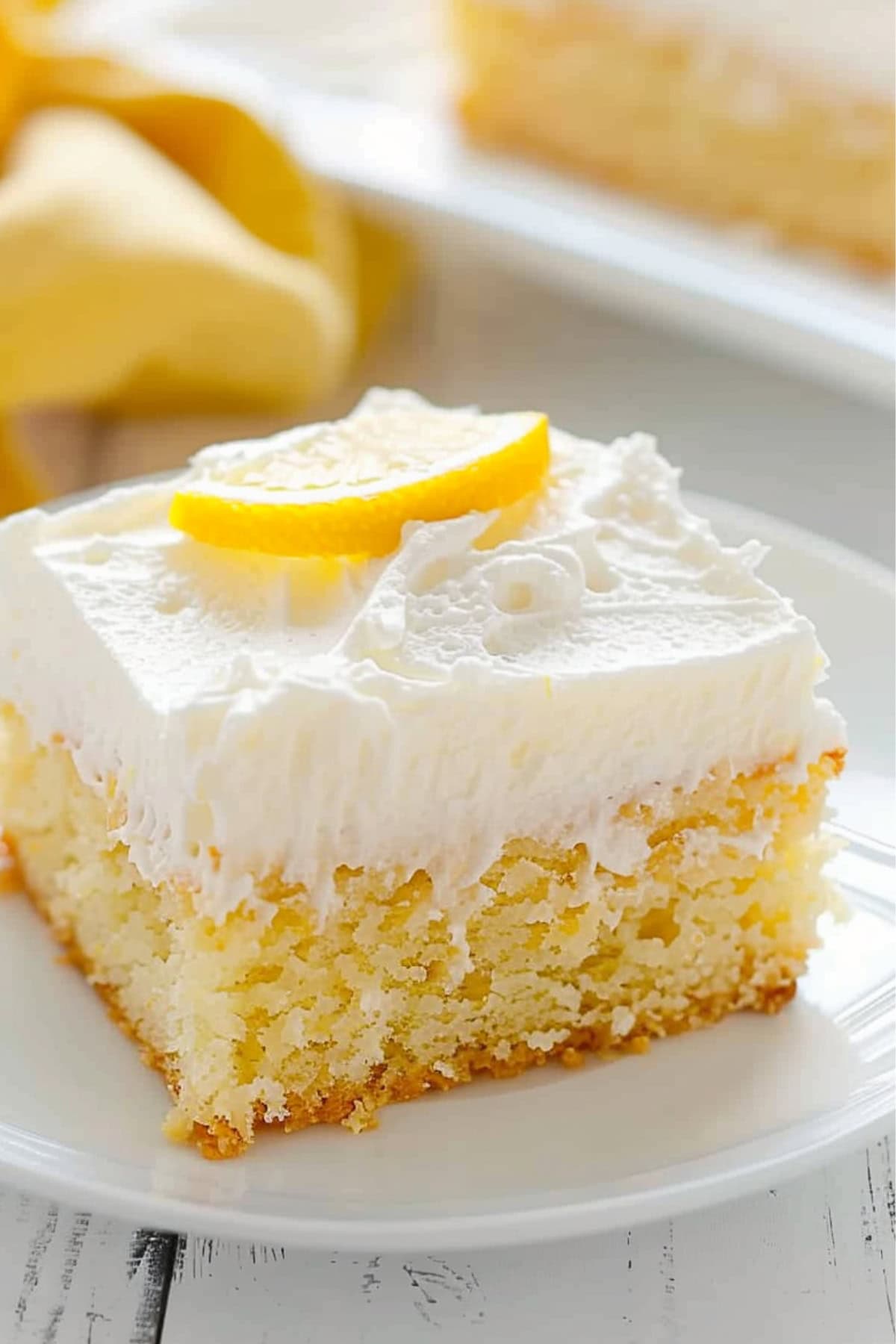 A slice of of lemon crazy cake with cream cheese garnished with lemon slice served on a white plate.