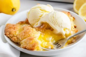 Lemon cobbler in plate with two scoops of vanilla ice cream.