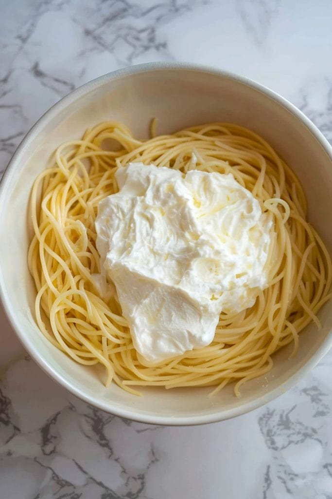 Spaghetti noodles in  a white bowl with cream cheese.