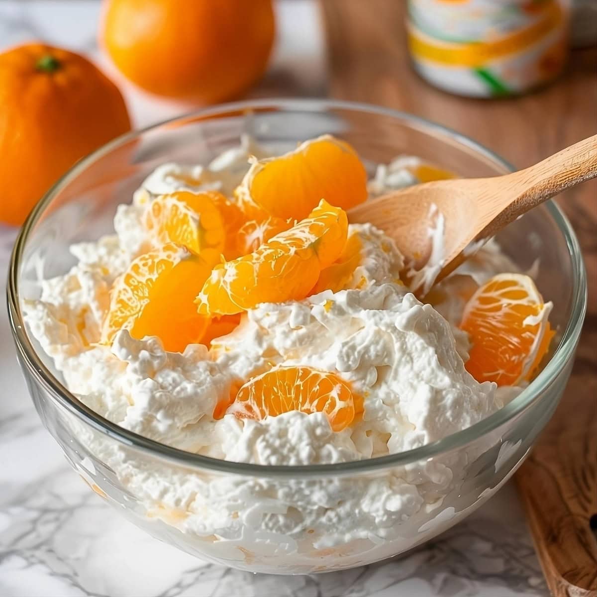 Oranges tossed in whipped cream in a glass bowl.
