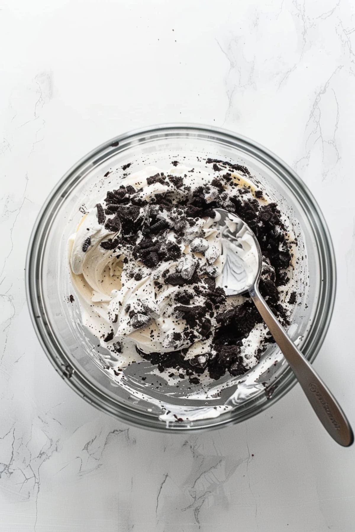A glass bowl of crushed Oreos with cream cheese dip on a white marble table