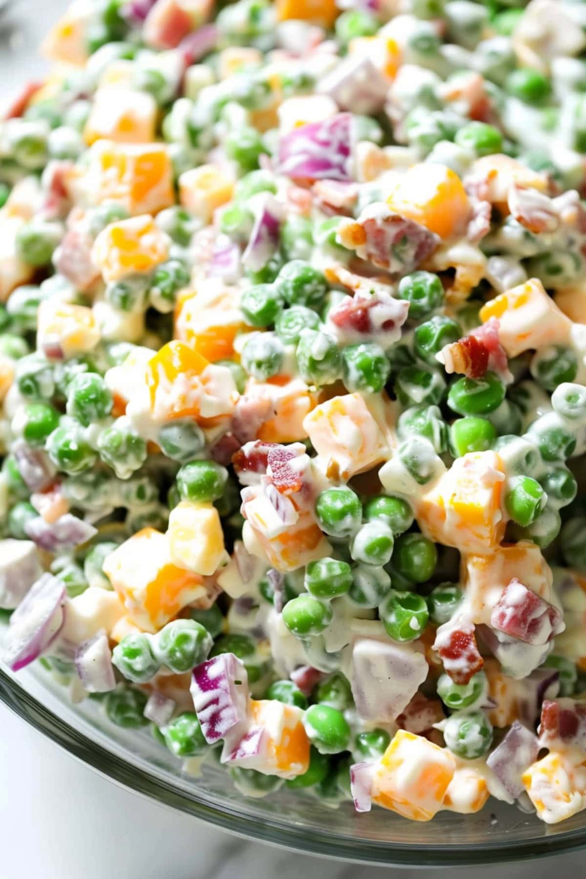 Creamy pea salad in a mixing bowl made with green peas, cheddar cheese, red onions and bacon with mayonnaise.