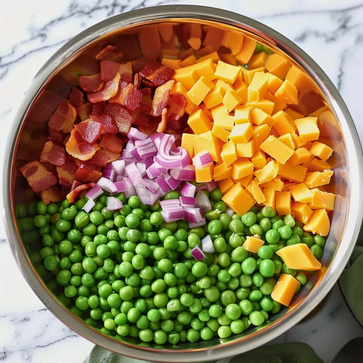 Pea salad ingredients, green peas, cheddar cheese cubes, bacon and red onions in a metal mixing bowl.