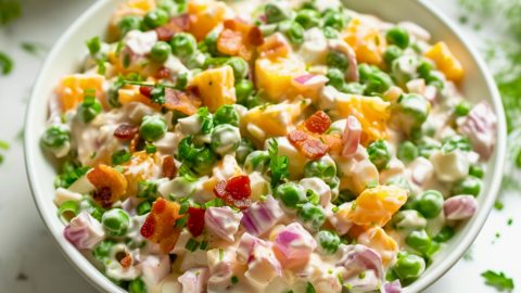 Pea salad in a white bowl loaded with cheese, bacon, green peas, and red onion in creamy mayonnaise dressing.