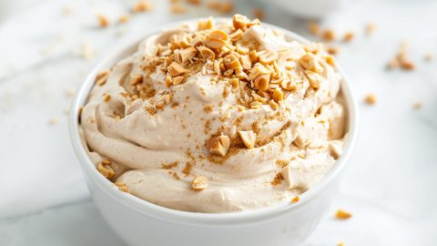 Fluffy and creamy peanut butter dip in a white bowl topped with chopped peanuts.