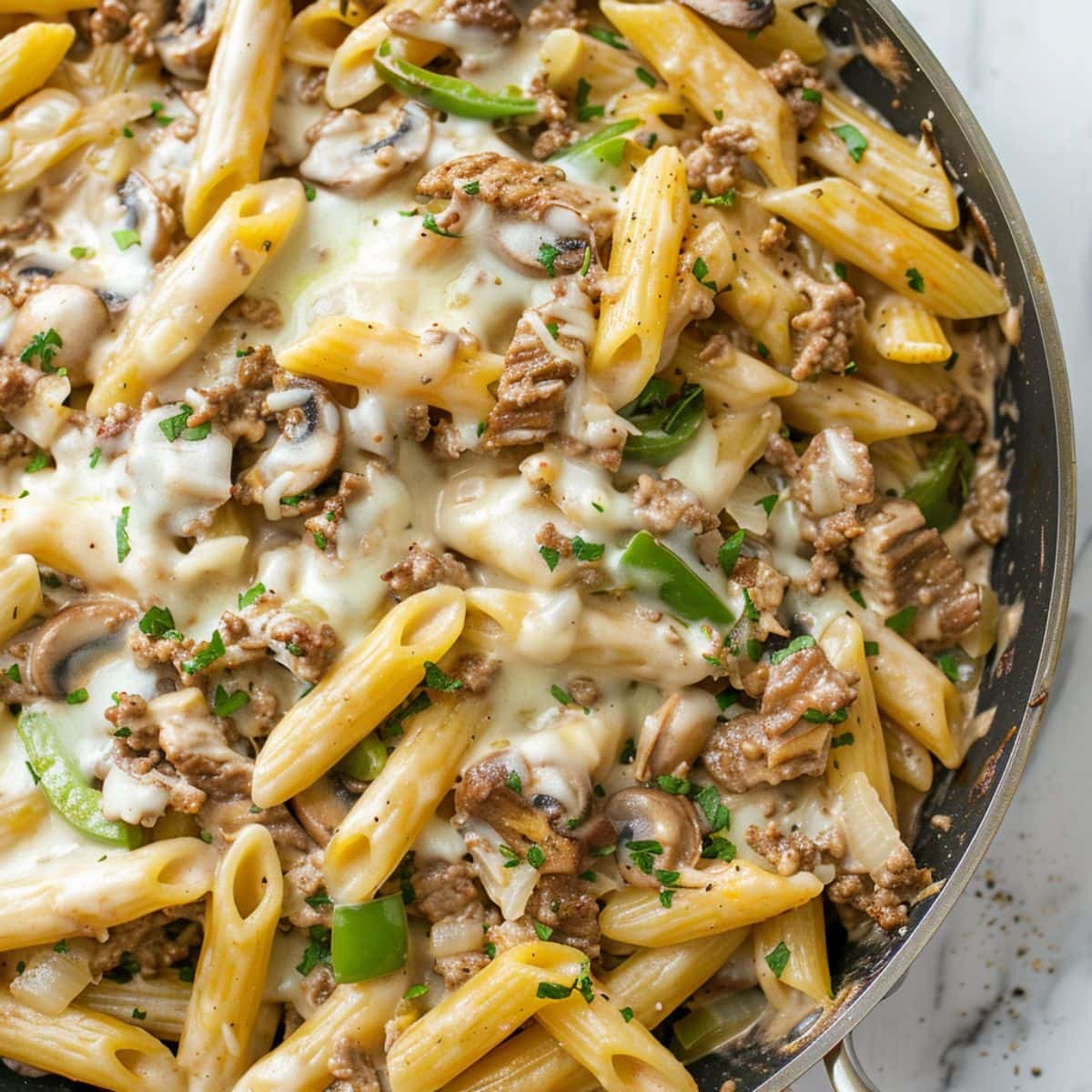 Philly Cheesesteak pasta in a cast iron skillet with sliced red bell pepper, beef and penne pasta in a creamy sauce.
