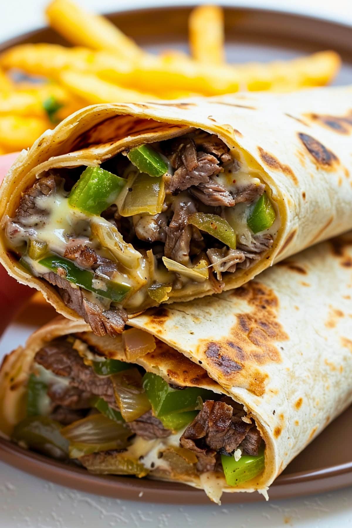 Stack of cheesesteak wrap and a portion of fries in a plate.
