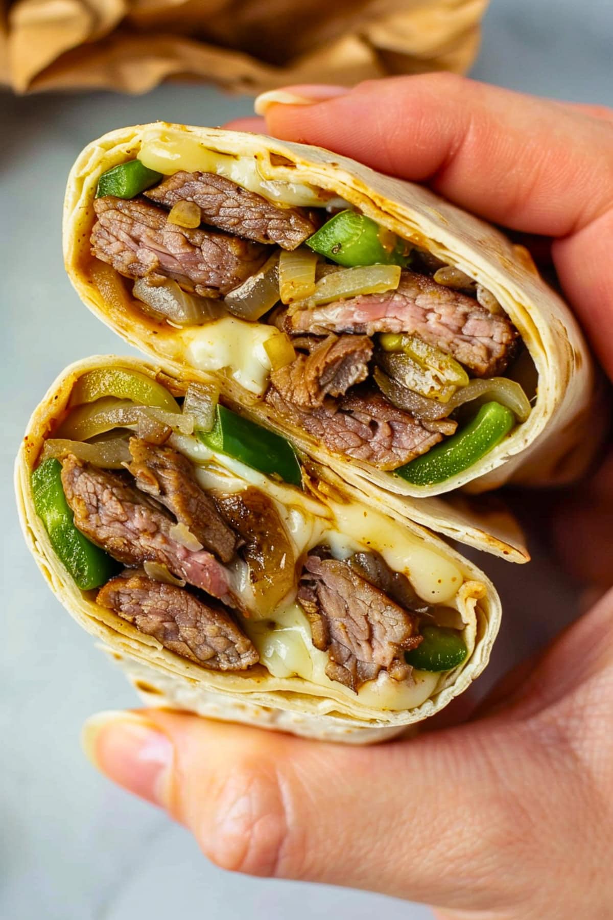 Hand holding Philly cheesesteak wrap.