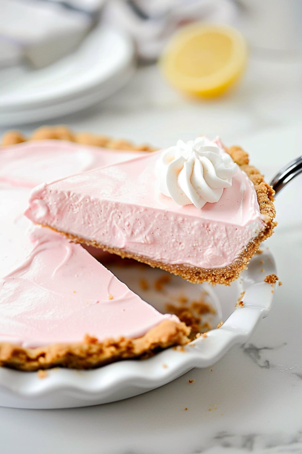 Pie ladle lifting a slice of pink lemonade piece with whipped cream on top.