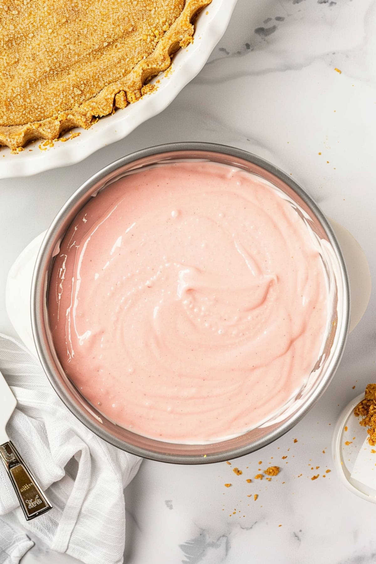 Pink lemonade pie filling in a stainless bowl with graham cracker crust on the side.
