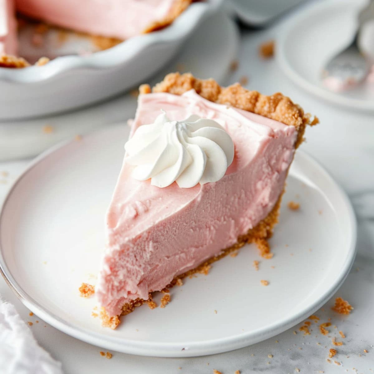 A slice of pink lemonade pie with whipped cream on top, served in a plate.
