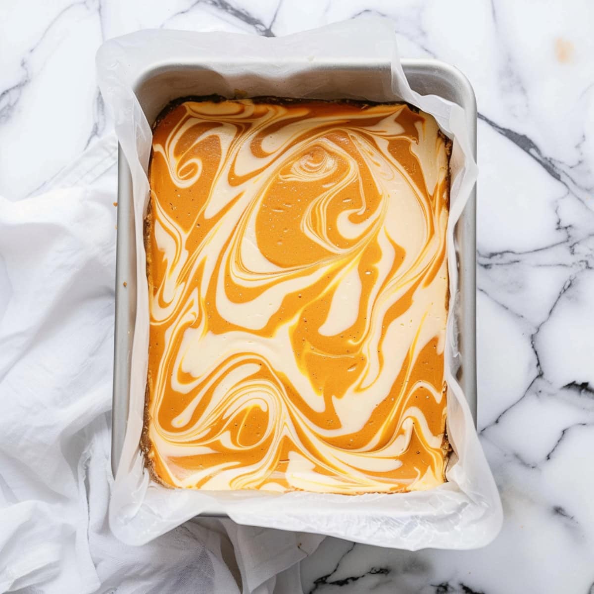 Pumpkin cheesecake swirled in a baking pan with parchment paper.