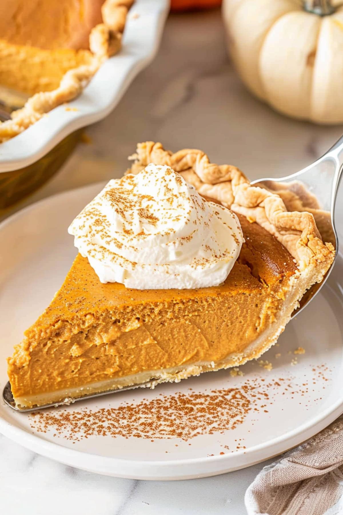 Pie ladle with a slice of pumpkin cream pie serving on a white plate.