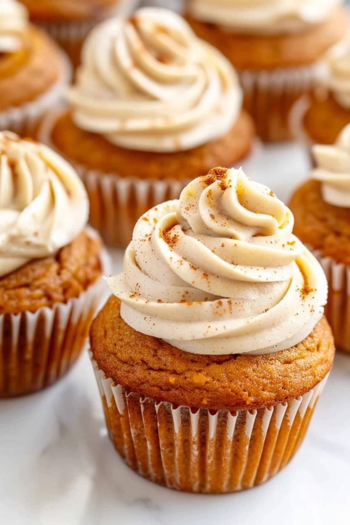 Pumpkin cupcakes on a white marble table topped with cream cheese frosting.