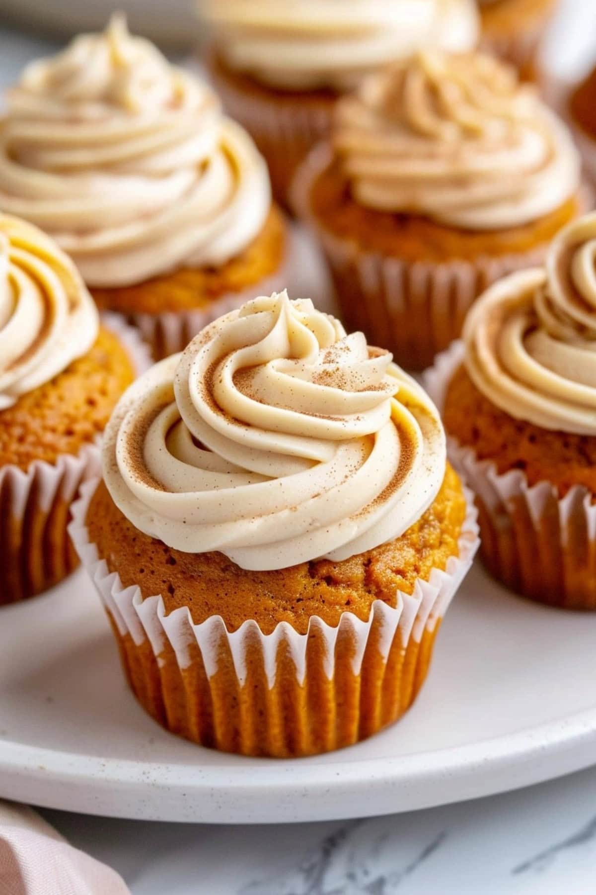 Pumpkin cupcakes with cream cheese frosting and sprinkle of pumpkin spice arranged in a white plate.