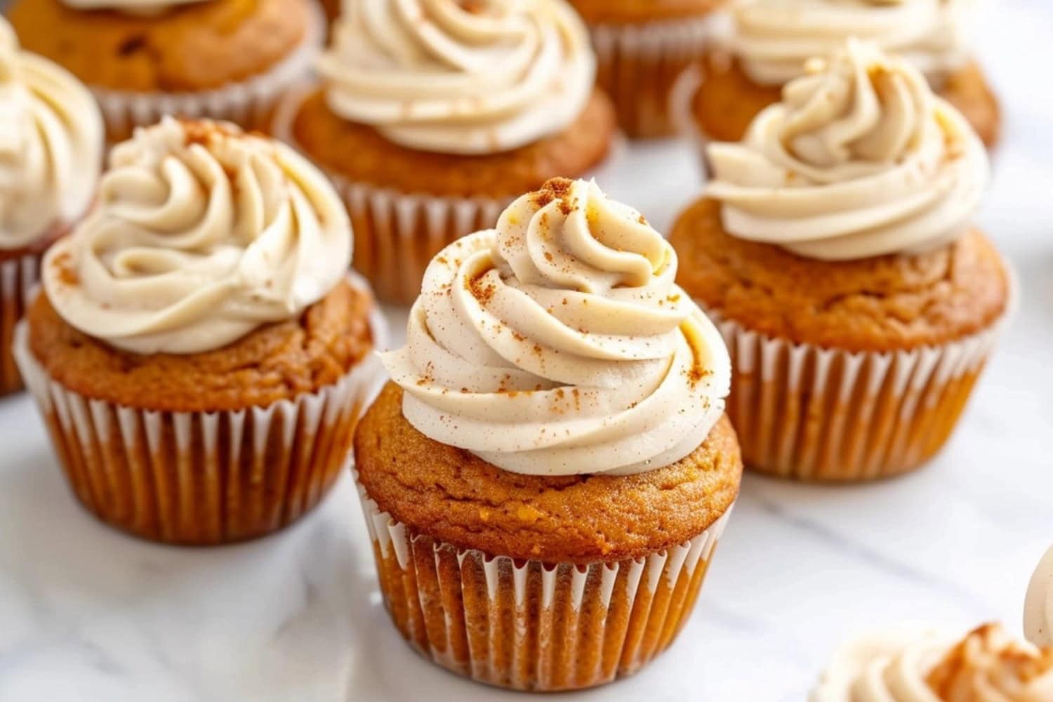 Pumpkin cupcakes with cream cheese frosting arranged in a white marble table.