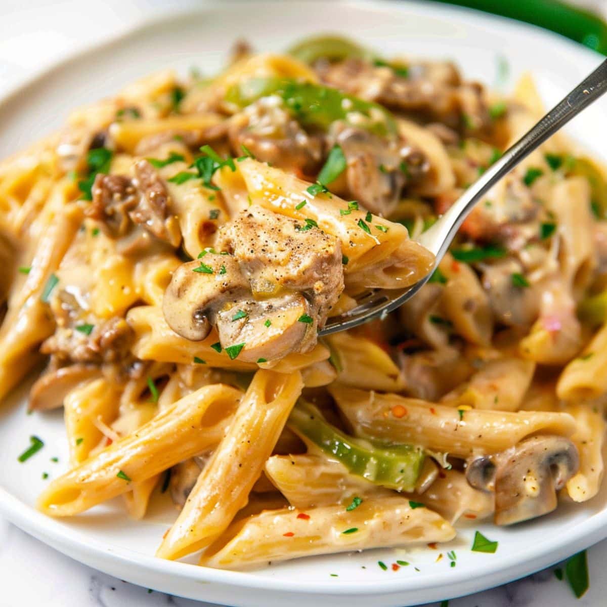 Fork lifting a portion of Philly cheesesteak pasta.