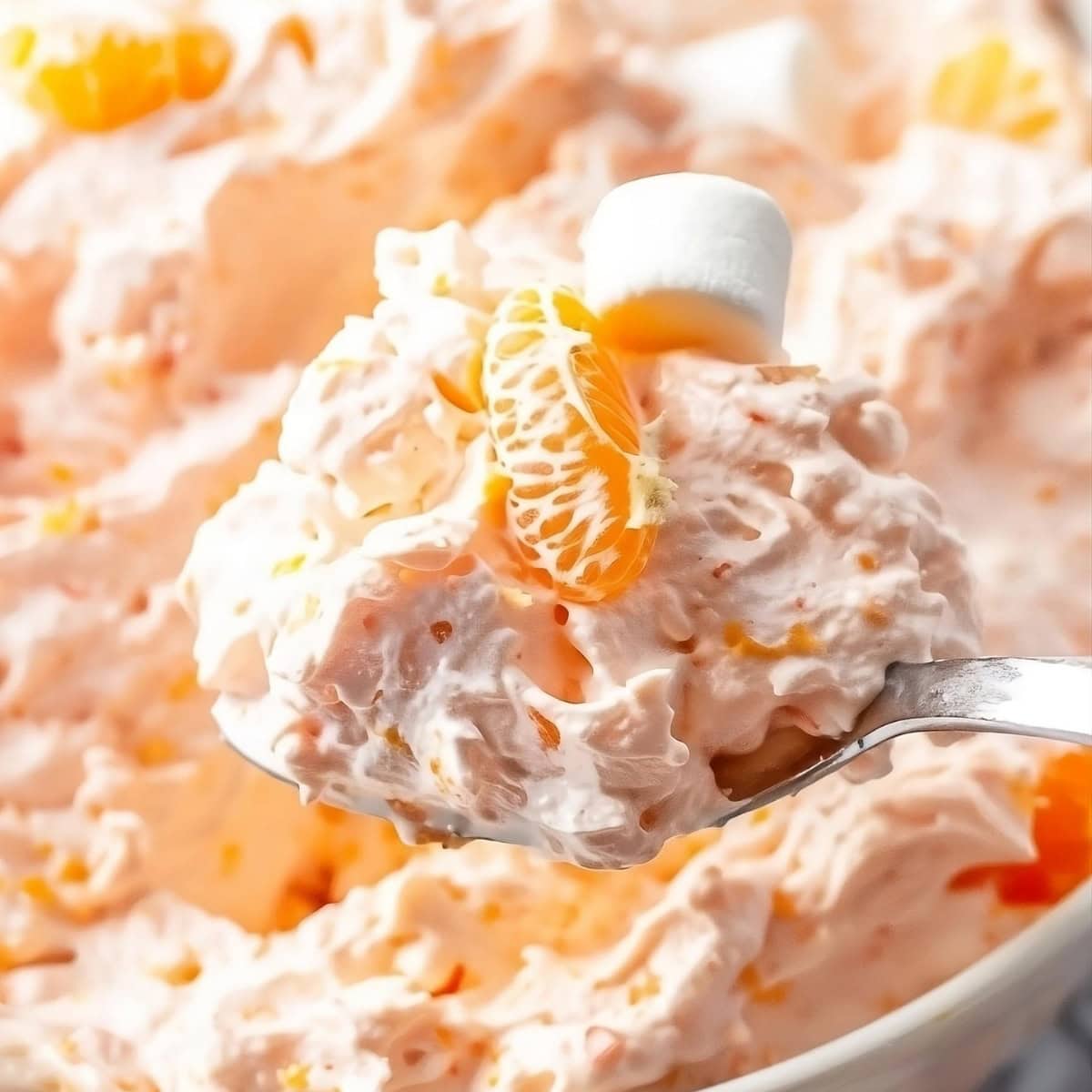 Spoonful of orange fluff salad garnished with marshmallow and fresh orange.
