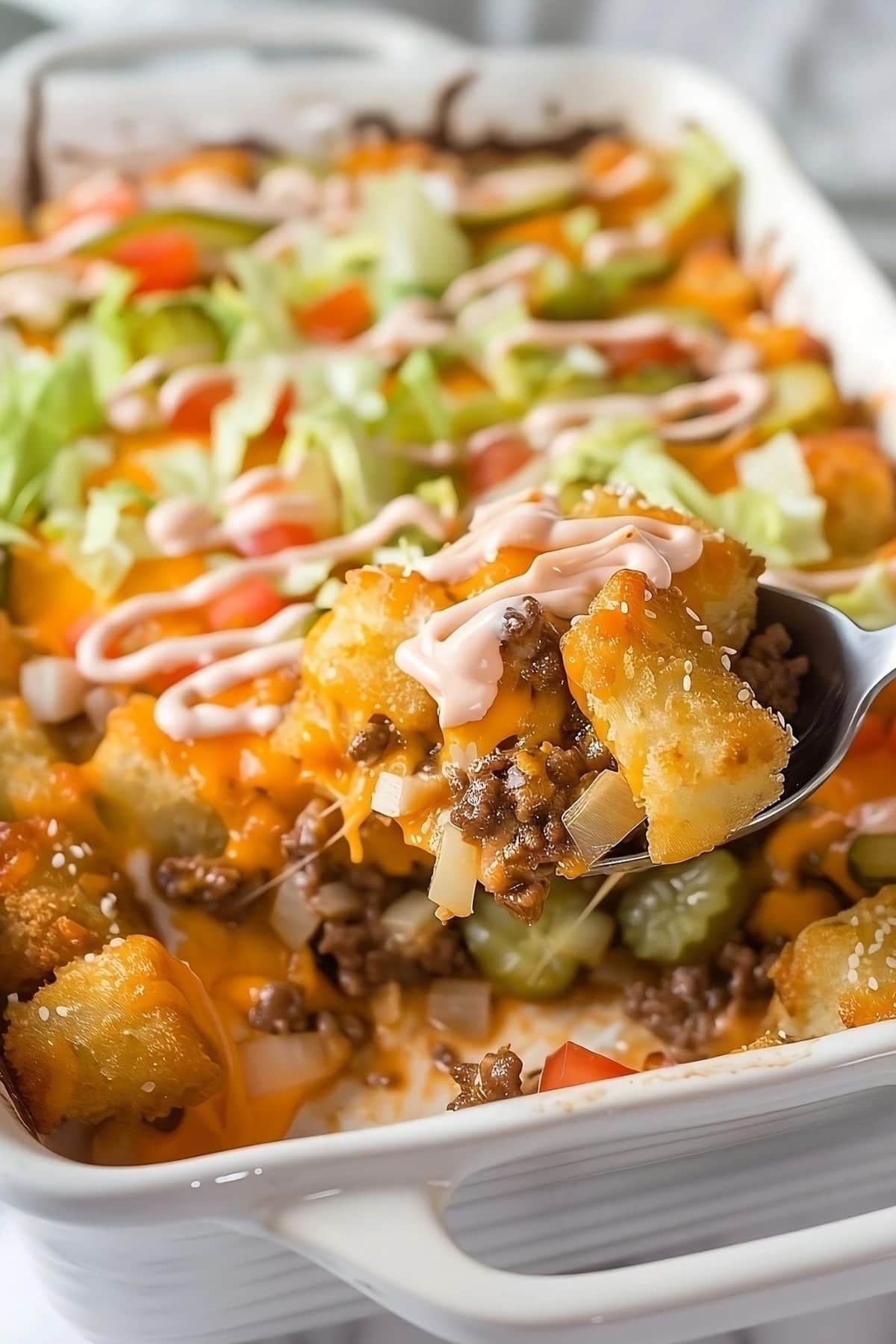 Spoon lifting a serving of Big Mac casserole with tater tots and ground beef. 