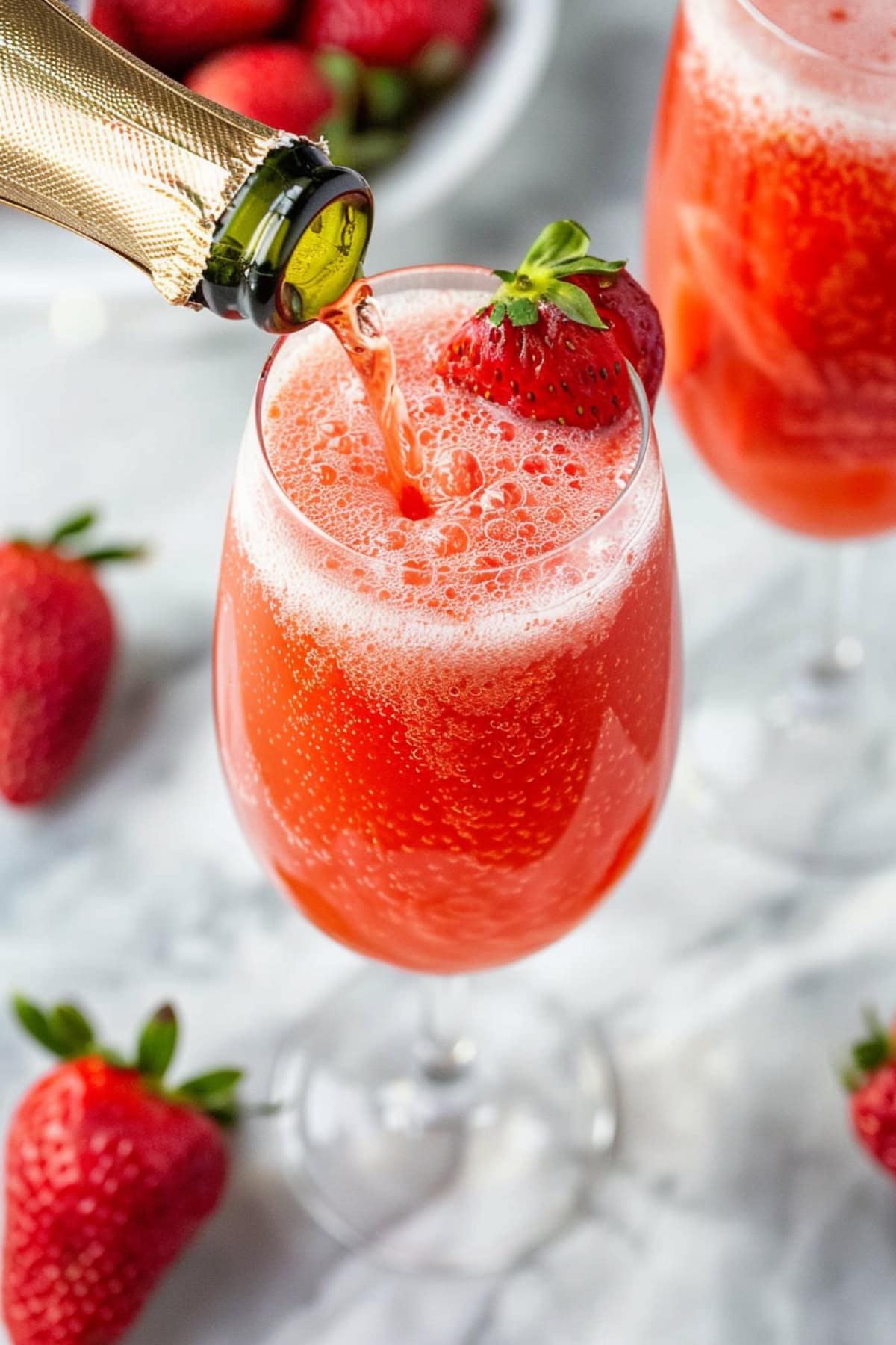 Glass of Strawberry berllini with sparkling wine pouring to it.