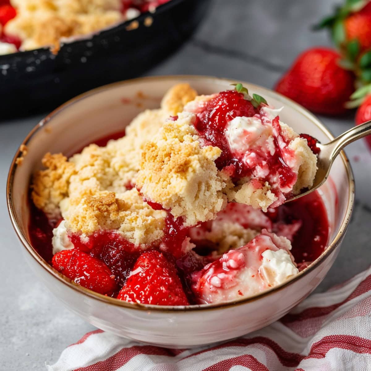 Strawberry Cheesecake Dump Cake scooping out of a bowl with fresh fruit