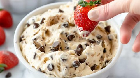 Fresh strawberry dipped in creamy chocolate chip cookie dough in a white bowl.