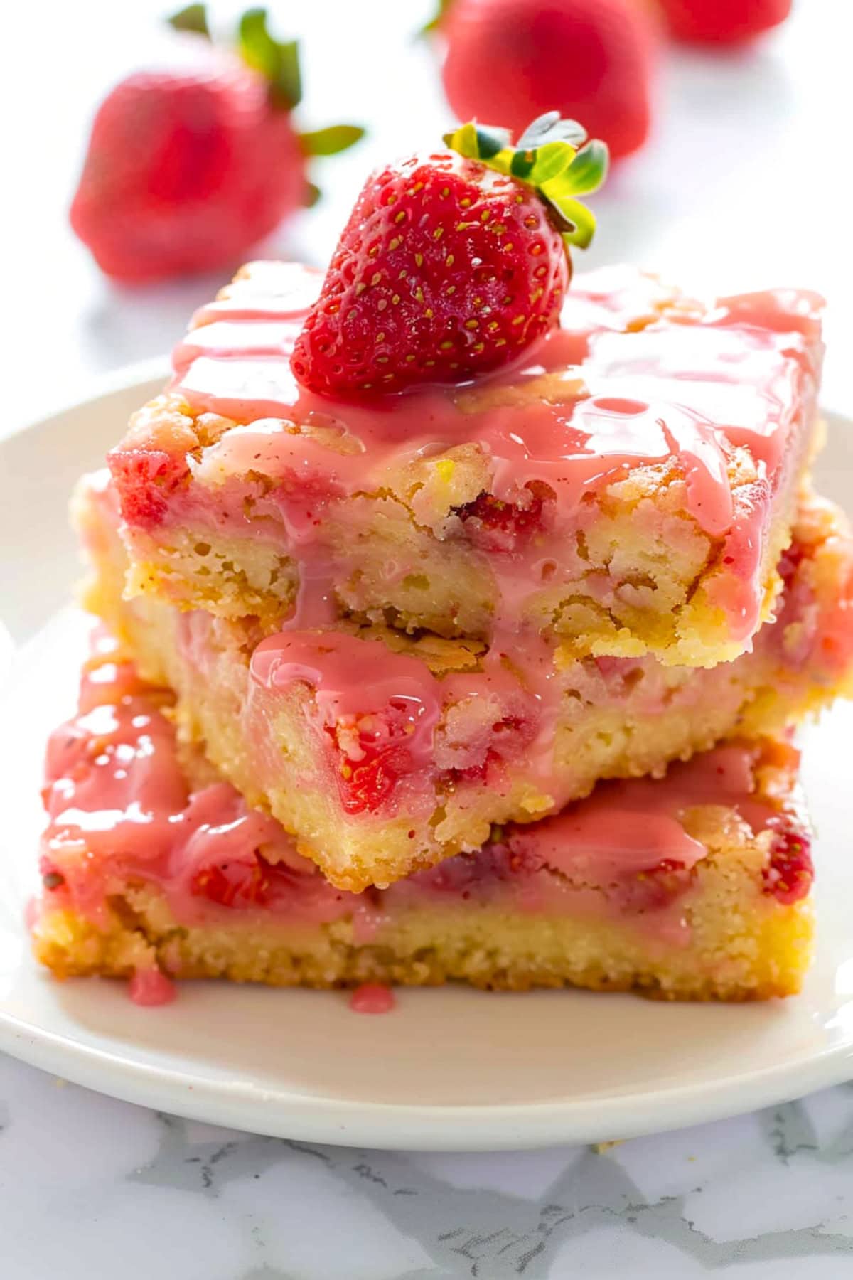 Strawberry lemon blondies on a white plate garnished with fresh strawberries and sweet glaze.