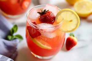 A refreshing summer drink: strawberry lemonade in a clear glass with ice and fruit garnish.