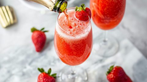 Sparkling wine pouring to a glass with strawberry puree garnished with fresh strawberries.