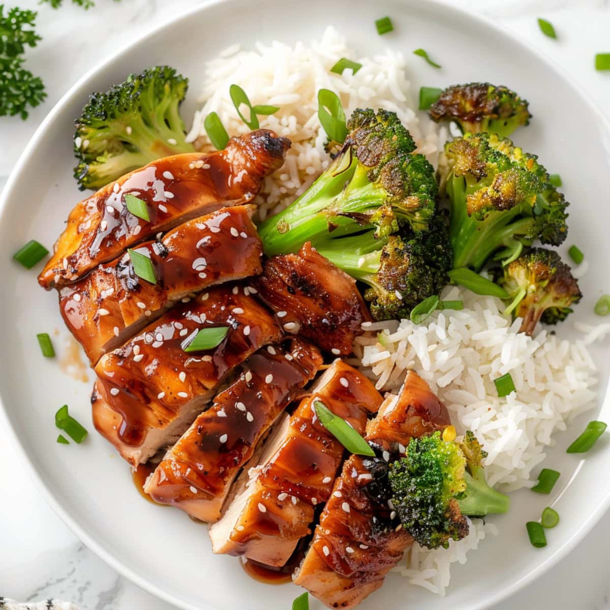Sliced teriyaki chicken served with rice and broccoli in white plate.