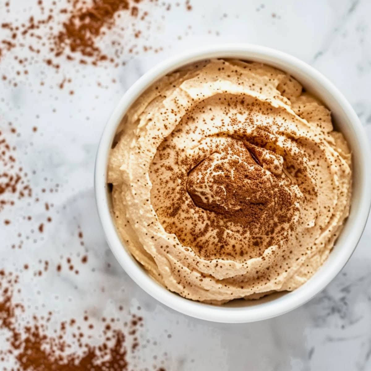 Tiramisu dip with cocoa powder on top in a white bowl, top down view