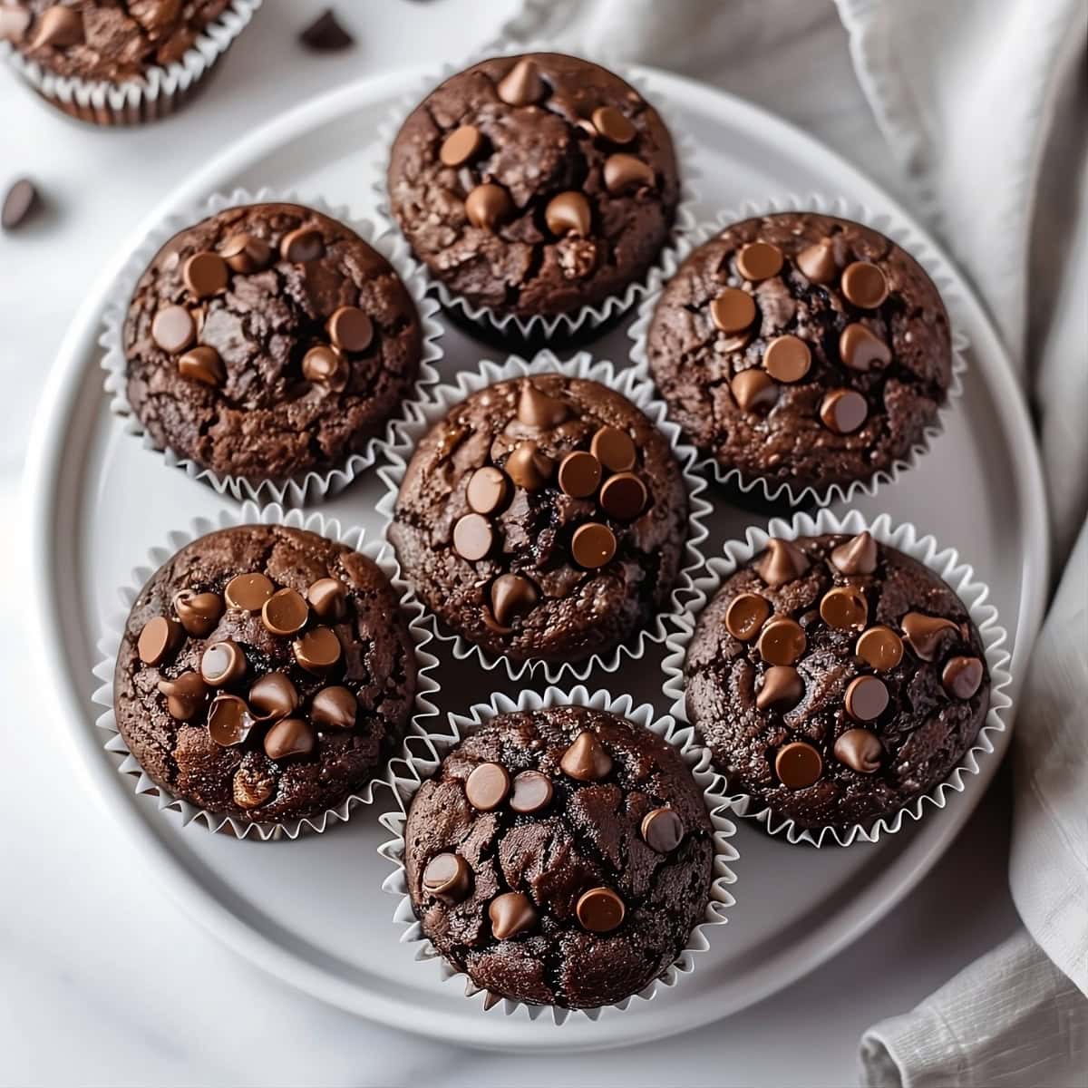 Bunch of triple chocolate muffins in a white plate, overhead shot topped with mini chocolate chips.